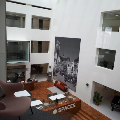 A modern office space rental in Mechelen Centrum featuring a bright, open atrium with a seating area and large artwork on the wall. Ideal office to rent for meetings or collaboration.