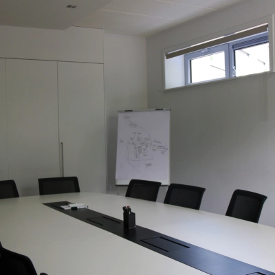 Conference room with a long white table, black chairs, and a flip chart in an office for rent at De Regenboog 11, Mechelen North.