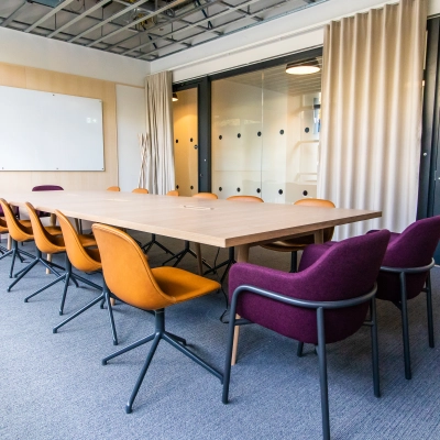 Modern conference room with a large wooden table and colorful chairs, ideal for office space rental in Munich Maxvorstadt.