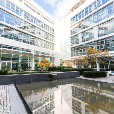 Exterior view of a modern office building at Oskar-von-Miller-Ring 20, Munich Maxvorstadt, featuring a courtyard with seating and water feature.
