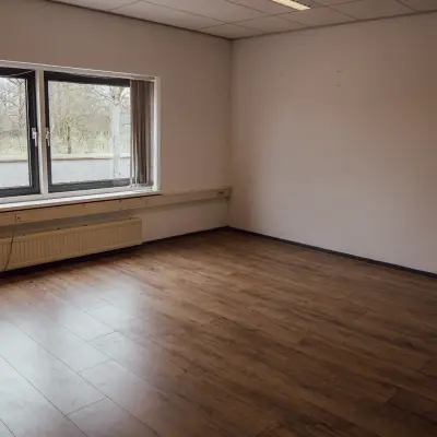 An empty interior space with wooden flooring and a large window, ideal for those seeking office space rental in Oosterhout Nb.