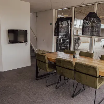 A furnished office space at Abdis van Thornstraat 74 in Oosterhout Nb, featuring a meeting table with chairs, a wall-mounted TV, and decorative lighting. Ideal for those looking to rent office space.