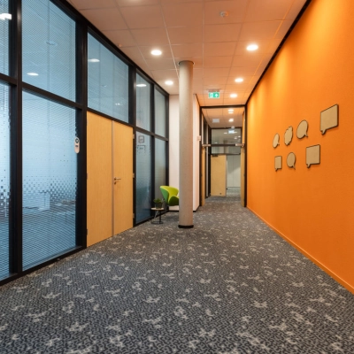 Bright office corridor at Veengang 1, Oosterwolde, ideal for office space rental, featuring vibrant walls and carpeted floors.