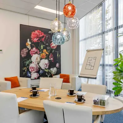 Bright and inviting conference room at Leeghwaterstraat 25 in Reeuwijk with a round table, modern pendant lights, and floral wall art. Ideal for office space rental.