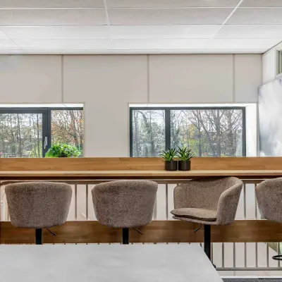 Modern office space with bar stools and plants, offering a scenic view through large windows.