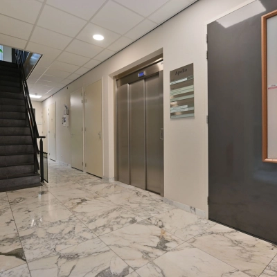 Interior view of an unfurnished office entrance at Laan van Vredenoord 17-19, featuring marble flooring, an elevator, and a staircase, ideal for office space rental.