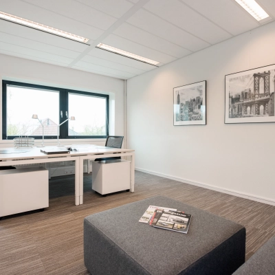 Bright office space with modern furnishings, featuring a large window and artwork on the walls. Ideal for office space rental.