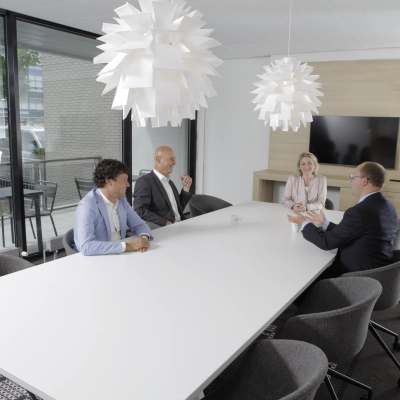 A furnished meeting room in an office space at Laan van Vredenoord 33, Rijswijk, with four people in business attire having a discussion around a white table. Ideal for office space rental.