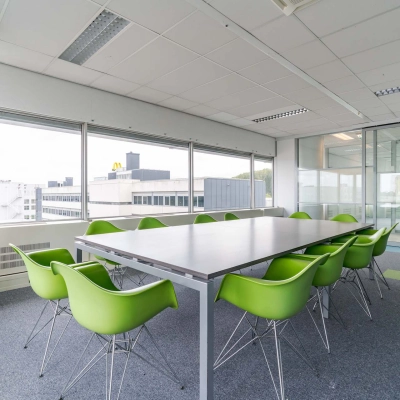 Bright office space for rent at Polakweg 7, Rijswijk, featuring a large meeting table surrounded by green chairs, ideal for collaborative work.