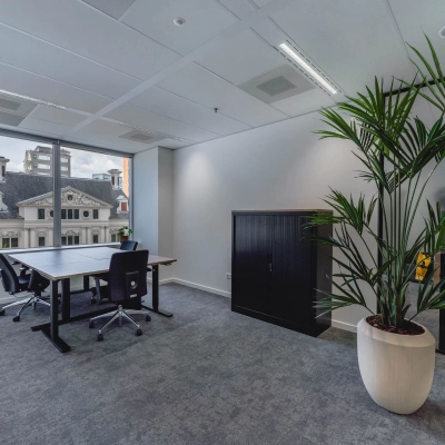Bright office space with large window view at Blaak 555, Rotterdam Center. Ideal for office space rental with modern furnishings and a potted plant.