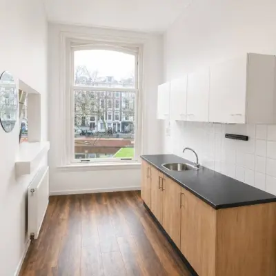 Bright, unfurnished office space at Mauritsweg 33 A01 in Rotterdam Center with hardwood floors, a large window, and a kitchenette, ideal for startups seeking office space rental.