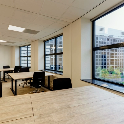 Spacious office space rental with large windows in Rotterdam Center, featuring wooden desks and rolling chairs, ideal for those looking to rent office space at Weena 335.