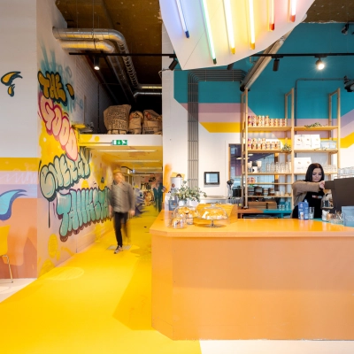 Vibrant interior at Weena 70, Rotterdam Center, featuring colorful decor and a café area where a person is preparing a beverage, ideal for office space rental.