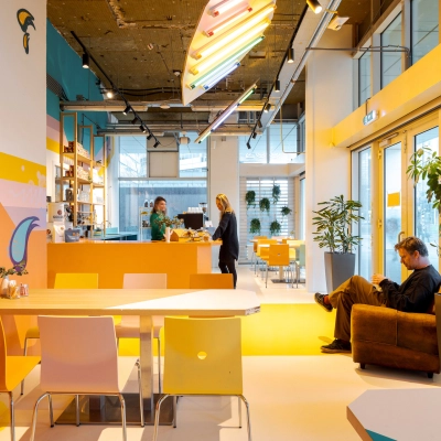 Lively office space at Weena 70, Rotterdam Center featuring a vibrant meeting and work area with people discussing and another person sitting. Ideal for office space rental.