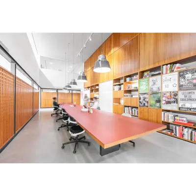 Spacious office space rental at Hofplein 20, Rotterdam Central Station, featuring a long table and shelves with books, ideal for collaborative work. Modern lighting and seating enhance the functionality.