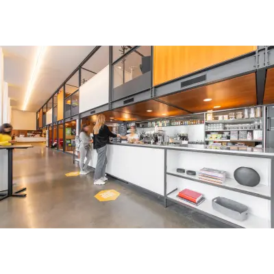 Modern office pantry at Hofplein 20, Rotterdam Central Station, featuring shelves with kitchenware, a coffee station, and people engaging in discussions. Ideal for rent office space enthusiasts.