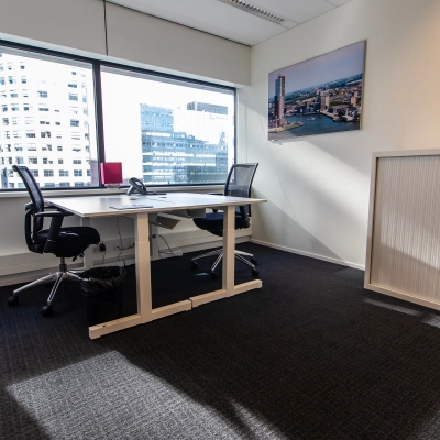 Bright office space at Weena-Zuid 130, Rotterdam Central Station, featuring two desks with black chairs, large window views, and minimalist decor. Ideal for office space rental.