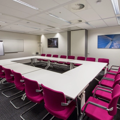 A furnished meeting room with a large U-shaped table and red chairs, perfect for office space rental at Weena-Zuid 130, Rotterdam Central Station.