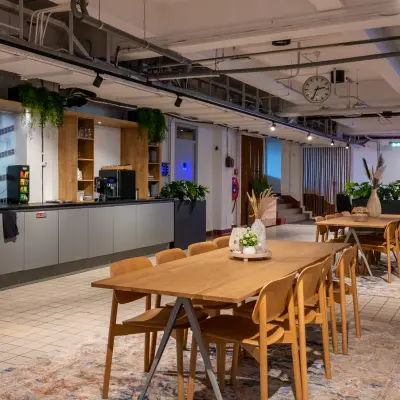 Spacious office interior at Van Nelleweg 1, Rotterdam Delfshaven, featuring modern wooden tables, chairs, and a coffee area for office space rental.