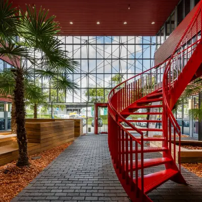Bright office space in Schiphol Airport with a striking red spiral staircase and indoor greenery.