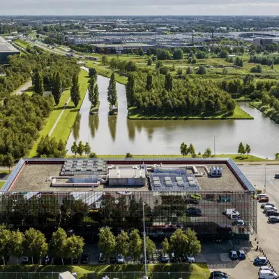 Aerial view of a modern office building surrounded by greenery and water at Schiphol Airport.