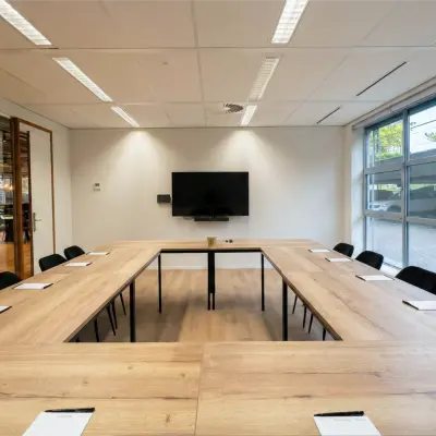 A bright conference room at Boeing Avenue 1-19, Schiphol Rijk, featuring a U-shaped wooden table, chairs, and a wall-mounted screen, ideal for office space rental.