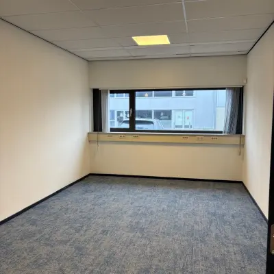 Unfurnished office space at Fischerpad 106 in Sittard available for rent, featuring blue carpet and wide windows.
