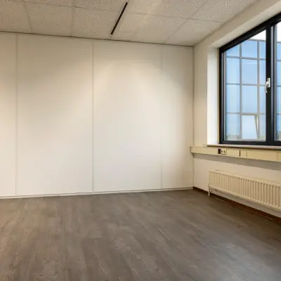 Empty office space with wooden flooring and a large window, available for rent at Curieweg 9, Spijkenisse.
