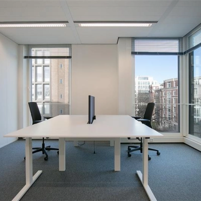 Modern office space rental at Alexanderveld 5-9, The Hague Center, featuring a bright workspace with large windows, two desks, and chairs, ideal for professional collaboration.