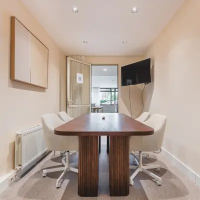 Cozy furnished office space for rent at Zeestraat 100 in The Hague Center, featuring a wooden table, chairs, wall-mounted TV, and natural lighting.