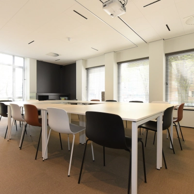 Bright office space rental in The Hague's Statenkwartier at President Kennedylaan 19, featuring a large meeting table and modern furnishings with natural light streaming through wide windows.