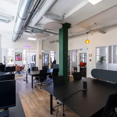 Furnished office space with sleek black desks and modern amenities at Oudegracht 161, showcasing a vibrant workspace ideal for rent in Utrecht Center, with professionals collaborating.