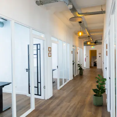 Bright office space with glass partitions at Oudegracht 161, Utrecht Center, available for rent. The hallway features wooden floors and modern lighting, leading to individual office rooms.