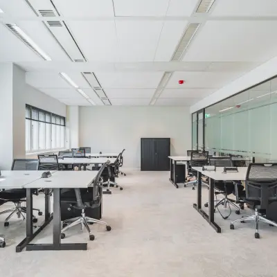 Modern office with glass partitions at Leiden Central Station for rent, featuring ergonomic chairs and ample desk space.