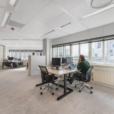 Office space at Utrecht Central Station with large windows, modern furniture, and professionals working at desks. Ideal for those seeking office space rental.