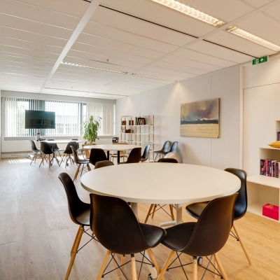 Modern office space for rent in Utrecht Lage Weide at Computerweg 22, featuring round tables, black chairs, and a wall-mounted TV, ideal for collaborative work.
