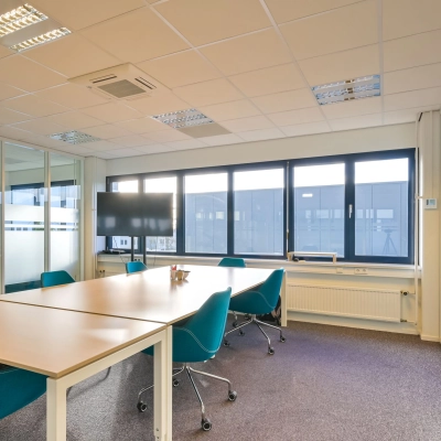 Bright and modern office space with large windows, furnished with a long wooden table and blue chairs, suitable for meetings or collaborative work.