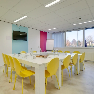 Bright office space for rent at Zonnebaan 18, Utrecht Lage Weide, featuring a meeting table with yellow chairs and natural light from a large window.