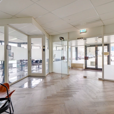 Bright office space at Zonnebaan 18, Utrecht Lage Weide with glass walls and wooden flooring, featuring a few chairs and a plant, ideal for office space rental.