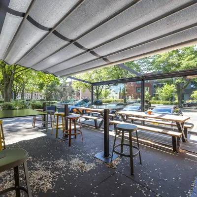 Outdoor office space with tables and stools under a retractable awning, suitable for rent at Goeman Borgesiuslaan 77 in Utrecht North.