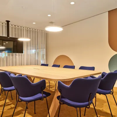 Bright conference room with modern wooden table, blue chairs, and a wall-mounted TV, perfect for office space rental or meetings at Van Deventerlaan 30-40, Utrecht Papendorp.