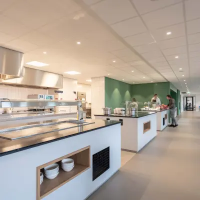 Spacious, modern office pantry at Van Deventerlaan 31-51, Utrecht Papendorp, with open food preparation area and seating, ideal for office space rental. People are serving food and dining.