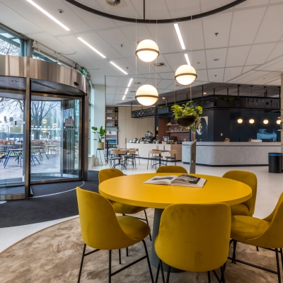 Modern office with round yellow table and chairs, attractive lighting, and reception area in the background, perfect for rent office space in Utrecht South.