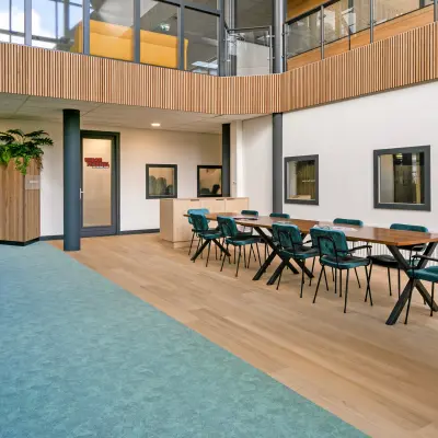 Modern office space rental featuring a spacious area with teal chairs and wooden table, surrounded by contemporary design elements at De Run 4312, Veldhoven.