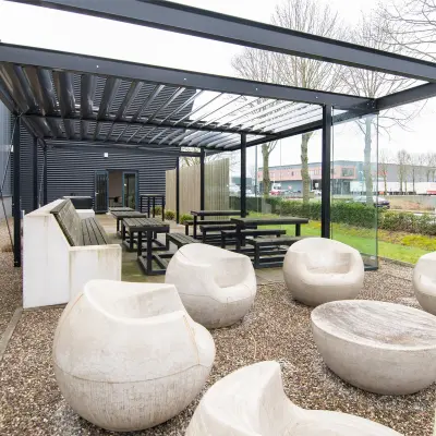 Outdoor seating area at Gildestraat 13 in Velp, ideal for office space rental with a mix of modern benches and sculptural chairs beneath a sleek pergola.