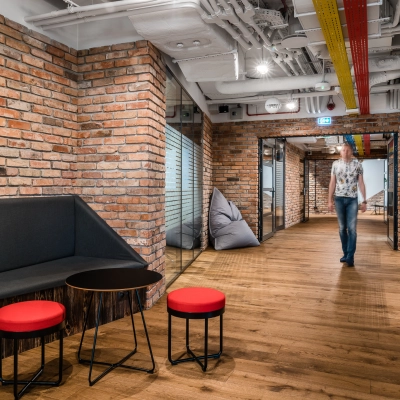 Modern office interior at Konstruktorska 11, Warsaw Mokotow, featuring brick walls, seating area, and a person walking, ideal for office space rental.