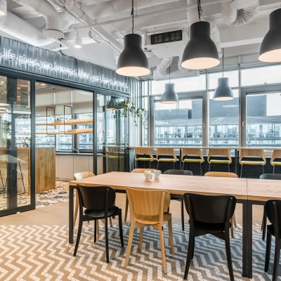 Modern furnished office space at Konstruktorska 11, Warsaw Mokotow with a communal table, high chairs by large windows, and contemporary lighting. Ideal office space rental for collaboration and creativity.