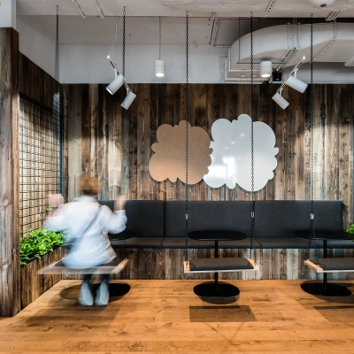 Modern office space with wooden walls at Konstruktorska 11, Warsaw Mokotow, featuring unique seating designs and plants, ideal for rent office space. A person is adjusting seating arrangements.