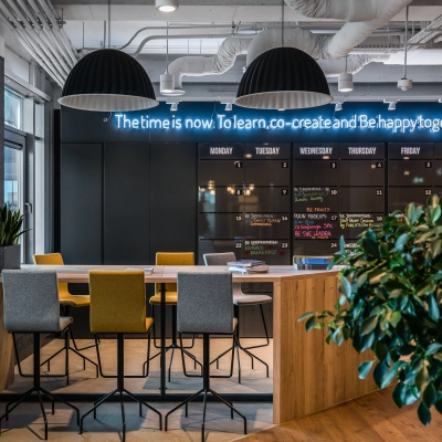 Modern workspace with high tables and chairs, accented by a neon sign, perfect for collaborative office space rental in Warsaw Mokotow.