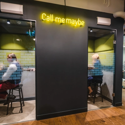 Two individuals work in private phone booths with glass doors in a modern office located at Konstruktorska 11, Warsaw Mokotow. Ideal office space rental for focused calls.